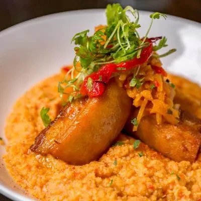 Plated dish: orange polenta-like base, golden pieces, and colorful garnishes.