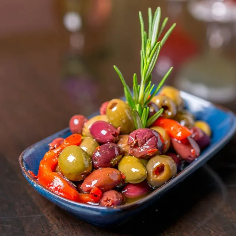 Rectangular blue bowl with assorted olives, red peppers, and rosemary sprig.