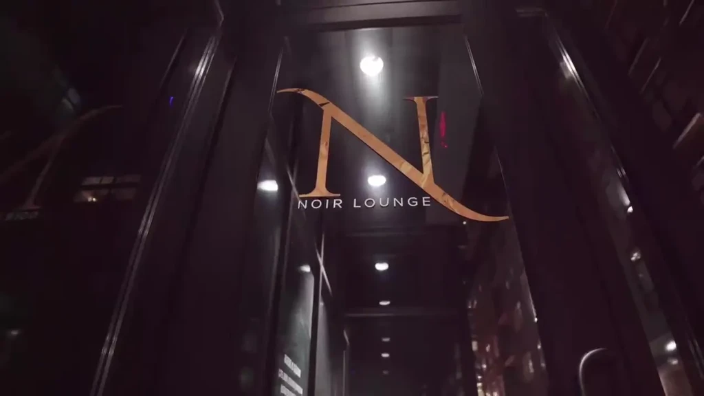 Large golden 'N' and "NOIR LOUNGE" sign on dark glass entrance.