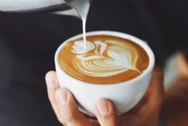 Hands pour milk into a latte cup, creating intricate latte art.