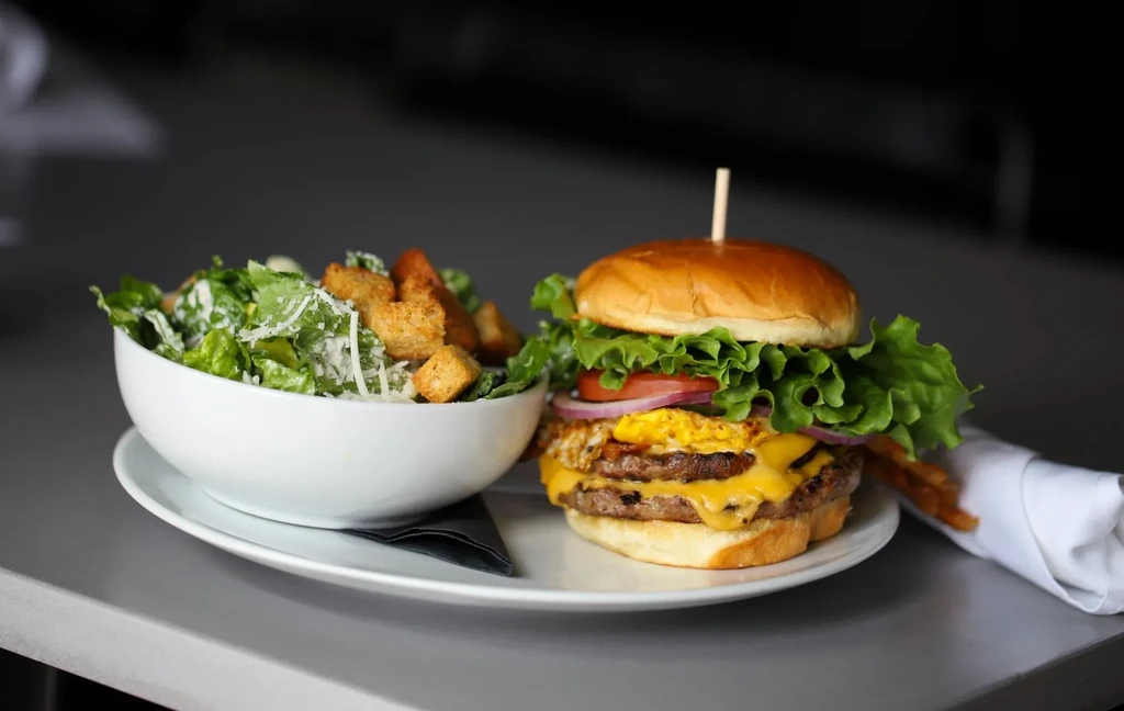 Close-up of a double-patty cheeseburger with fried egg and Caesar salad.