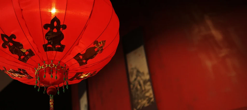 Illuminated red paper lantern with black patterns and green tassels.