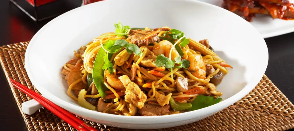 Close-up of colorful stir-fried noodles with meat, shrimp, and vegetables.