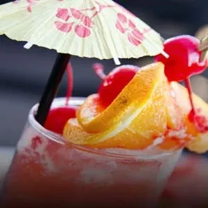 Reddish-pink cocktail with orange, cherries, and a floral umbrella.