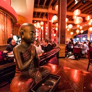 Bronze Buddha statue meditating in a vibrant restaurant with red lighting.