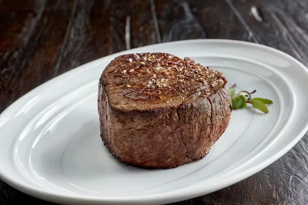 Seared, seasoned steak with green herbs on a white oval plate.