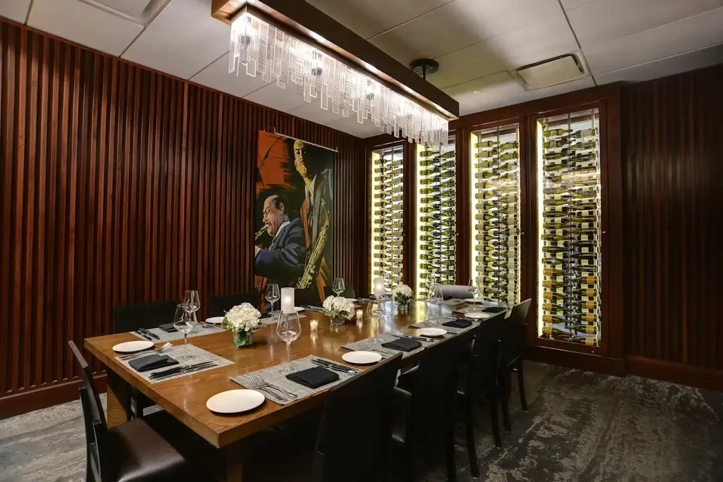 Elegant private dining room with long set table, wine racks, and saxophone painting.