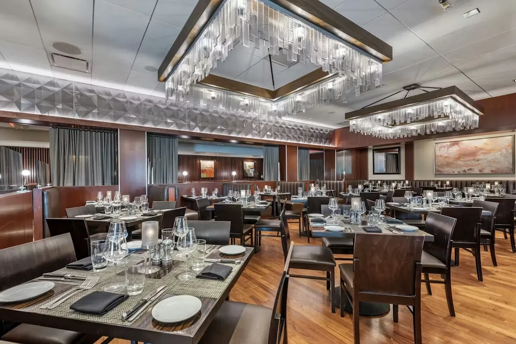 Upscale restaurant dining room with meticulously set tables and modern chandeliers.