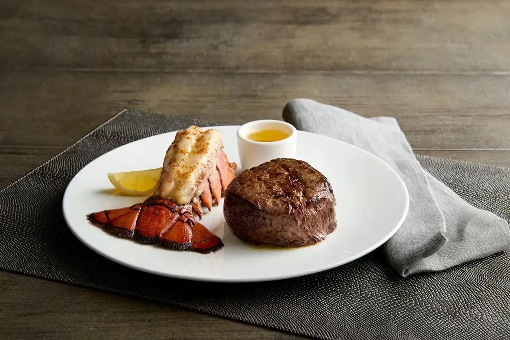 Grilled lobster tail and seared steak with lemon wedge.