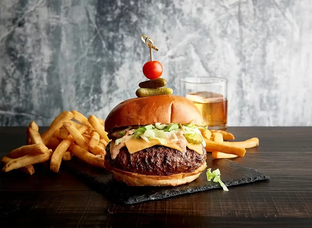 Gourmet cheeseburger and fries on a black slate board with a drink.