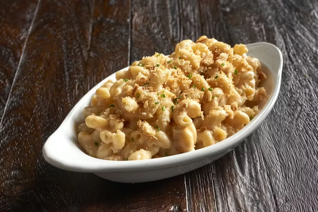 Creamy macaroni and cheese topped with breadcrumbs and herbs on wood.