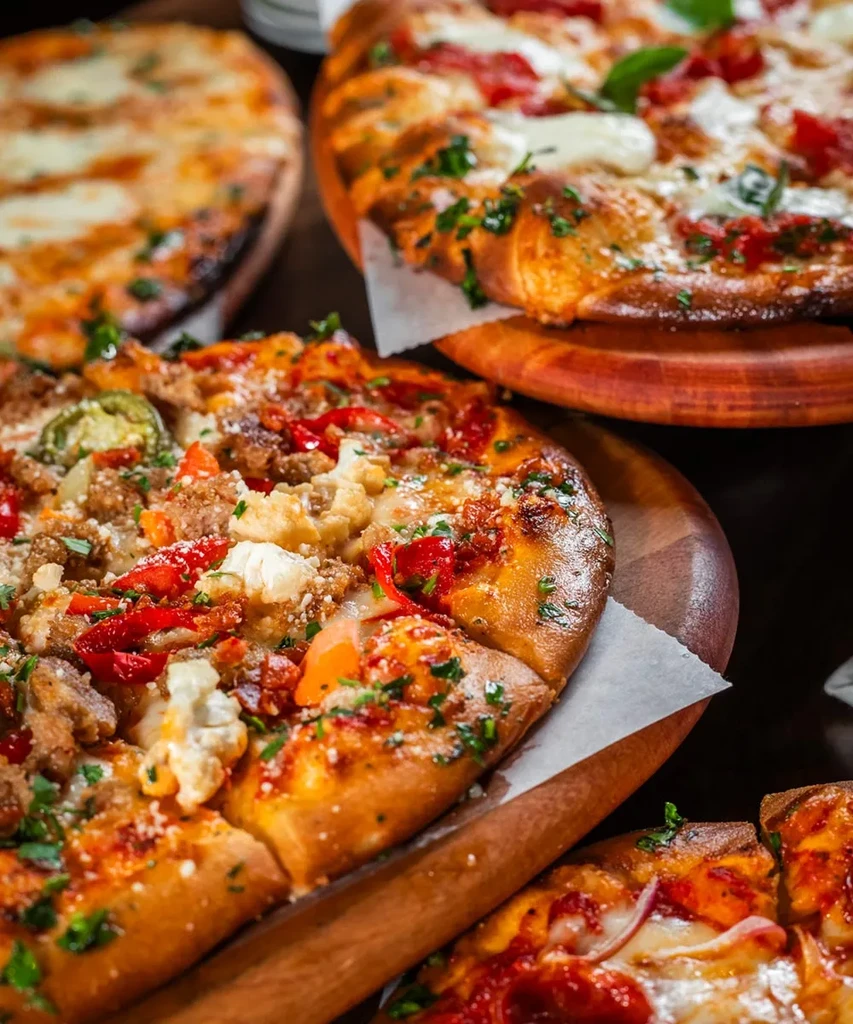 Top-down view of multiple pizzas on wooden boards: sausage and Margherita.