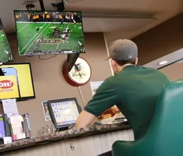 Person in green polo at counter with POS, watching football.