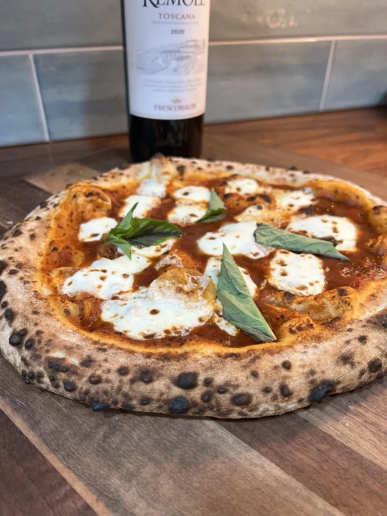 Close-up of Margherita pizza next to a bottle of Remole Toscana wine.