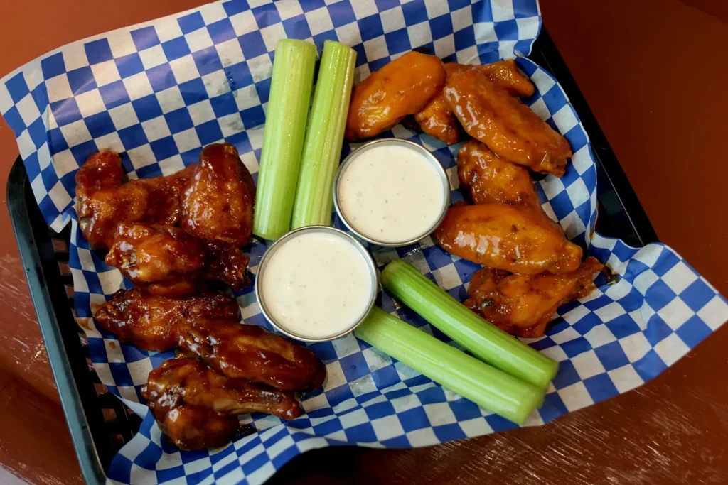 Sauced chicken wings, celery sticks, and dip in a checkered basket.
