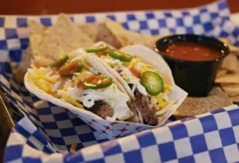Two street tacos with meat, cheese, jalapeños, chips, and salsa.