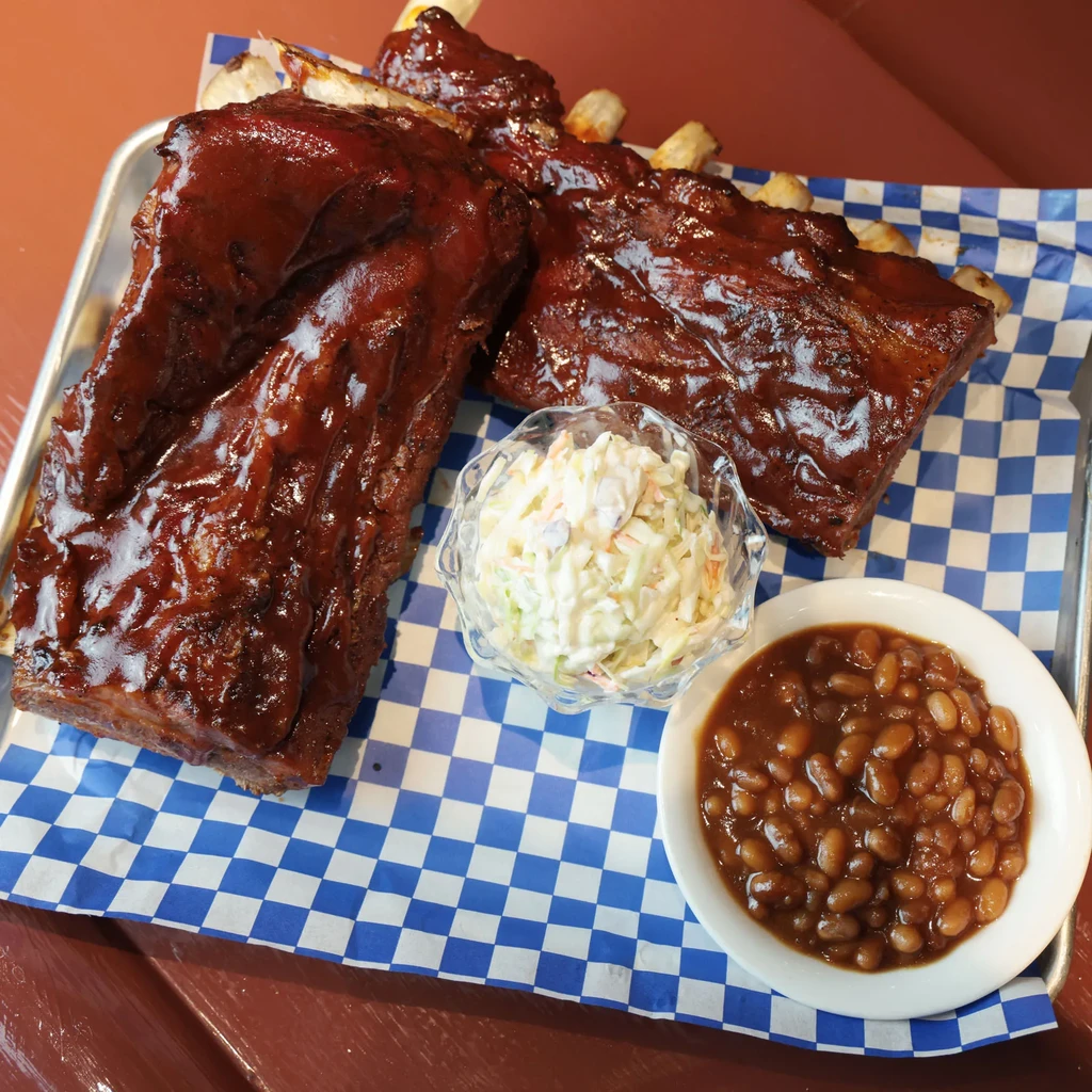 Two large portions of saucy BBQ ribs with coleslaw and baked beans.
