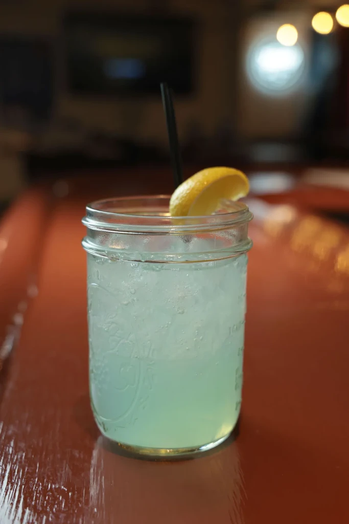 Blue-green drink in mason jar with crushed ice, straw, lemon wedge.