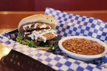 Stacked burger with fried green tomatoes and baked beans in a basket.