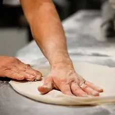 Hands kneading light dough on a floured kitchen surface.