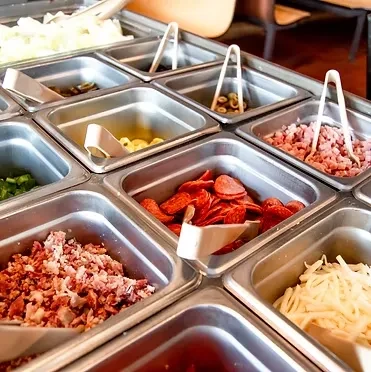 Restaurant food bar with bins of peppers, olives, macaroni, pepperoni, cheese.