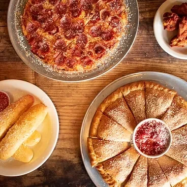 Overhead: pepperoni pizza, breadsticks, calzone, and wings on a rustic wooden table.
