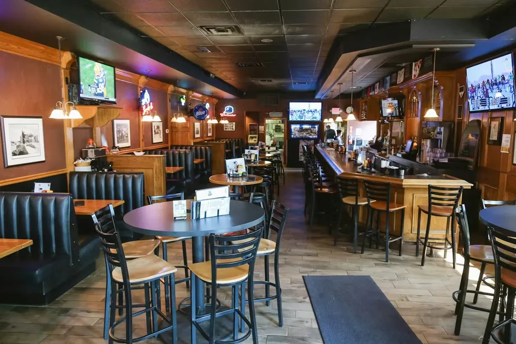 Interior of a casual sports bar with seating, prominent bar, and TVs.