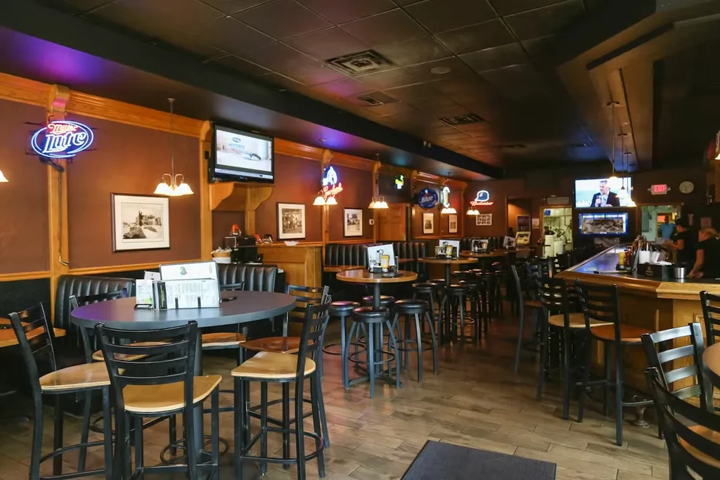 Casual bar interior featuring high-tops, booths, neon signs, and a long bar.