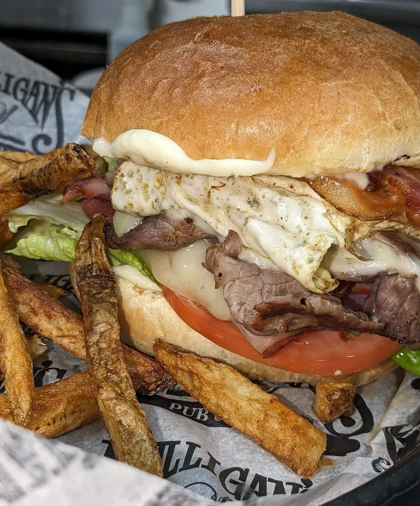 Close-up of a stacked burger and fries in a "MULLIGANS PUB" basket.