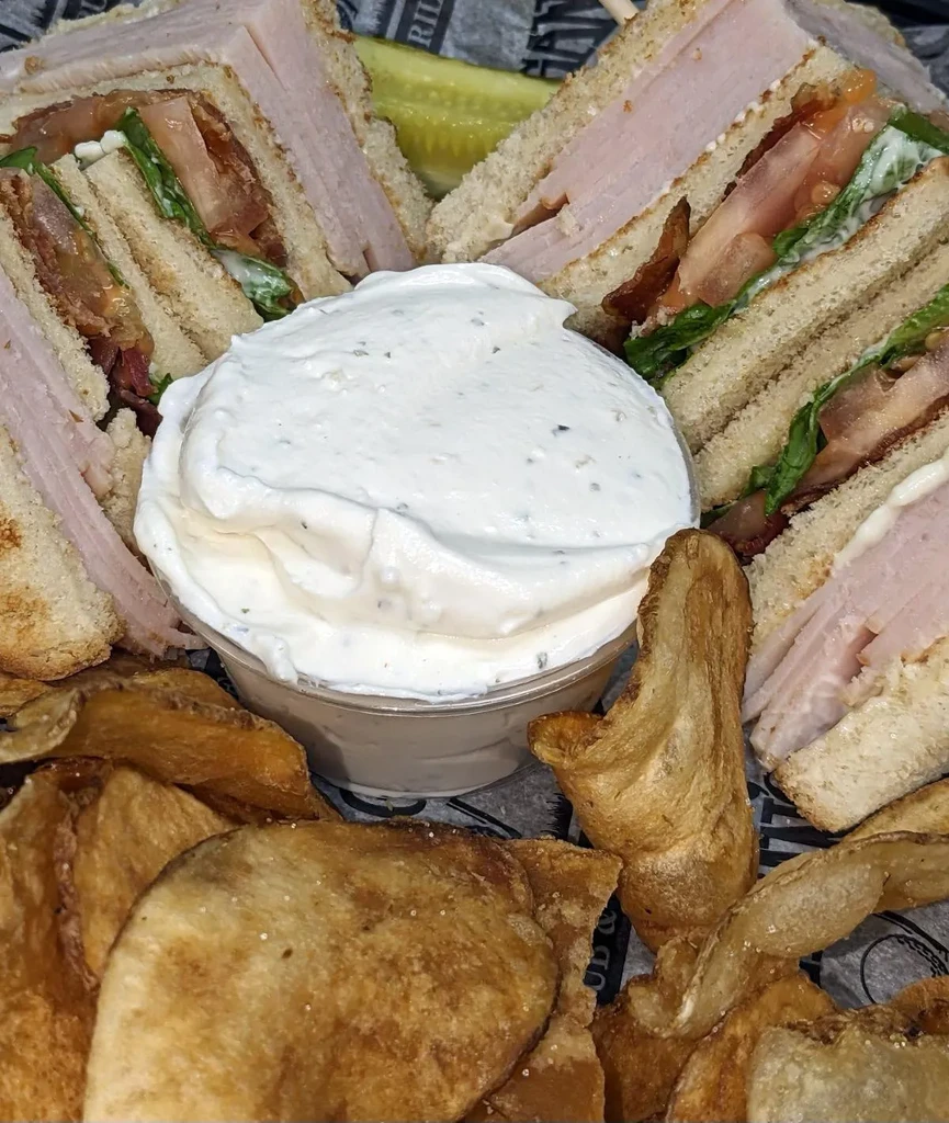 Club sandwich quarters, potato chips, creamy dip, and pickle spear.