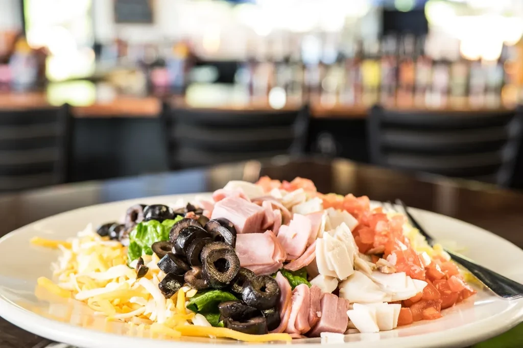Colorful chef's salad with ham, chicken, cheese, olives, lettuce, tomatoes.