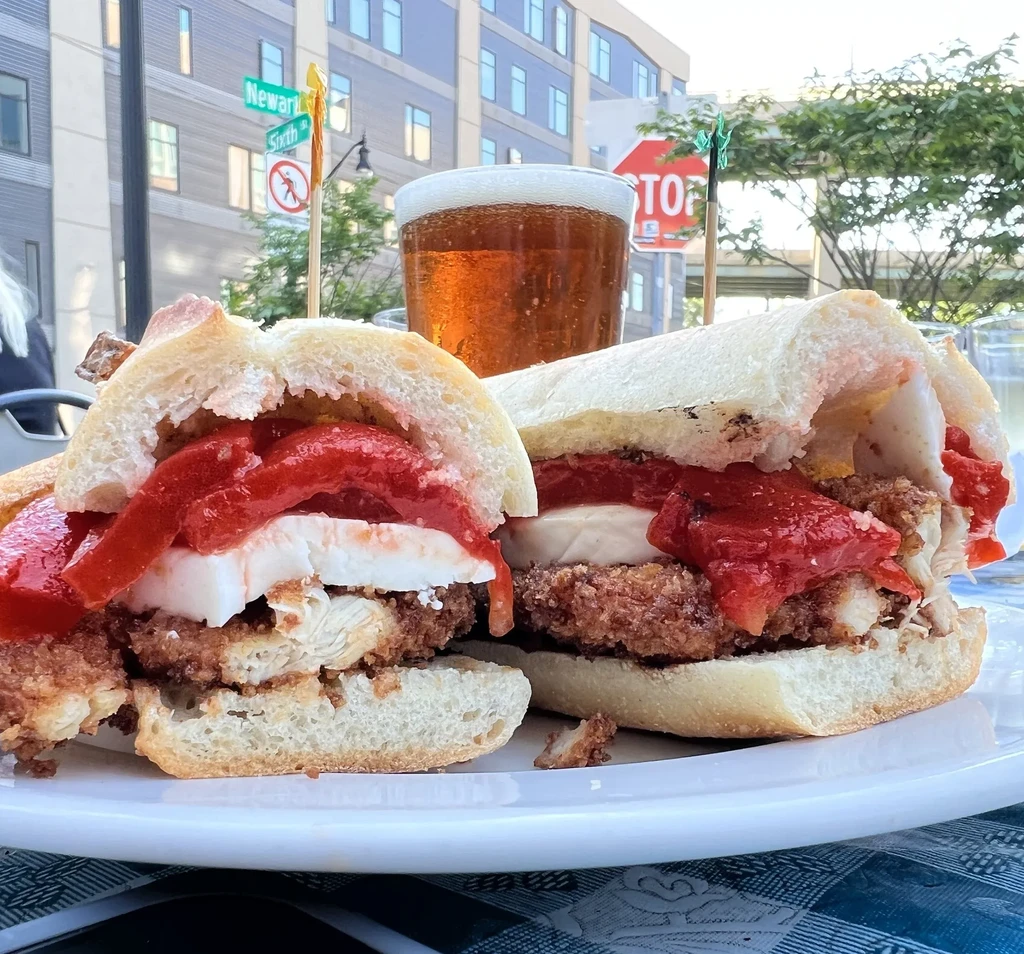 Two crispy chicken sandwiches with fresh mozzarella, red peppers, and beer.