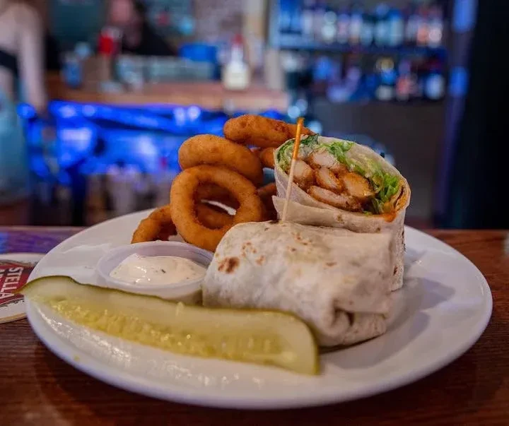 Chicken wrap, onion rings, dill pickle, and sauce on a plate.