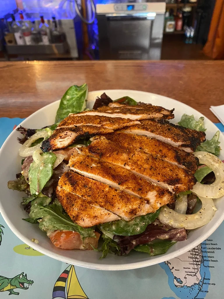 A grilled chicken salad with greens and onions on a tropical placemat.