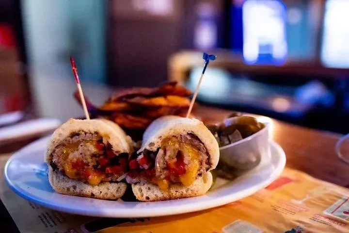Two slider sandwiches with fries and pickles on a white plate.