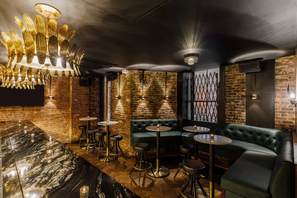 A dark, chic bar with brick walls, emerald banquettes, and golden lighting.