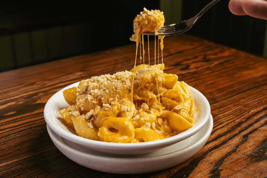 A fork lifts a cheesy noodle from a bowl of mac and cheese.