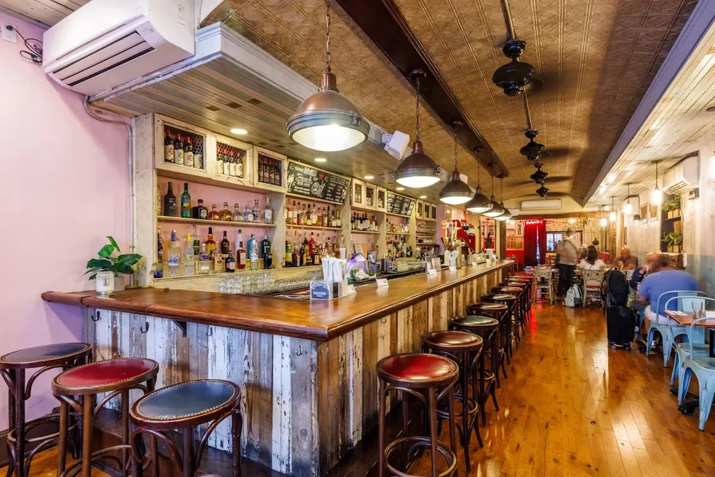 A long wooden bar with stools and shelves of liquor bottles.