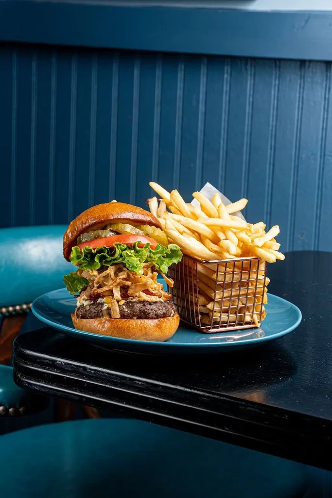 Gourmet burger with fries in a wire basket on a blue plate.