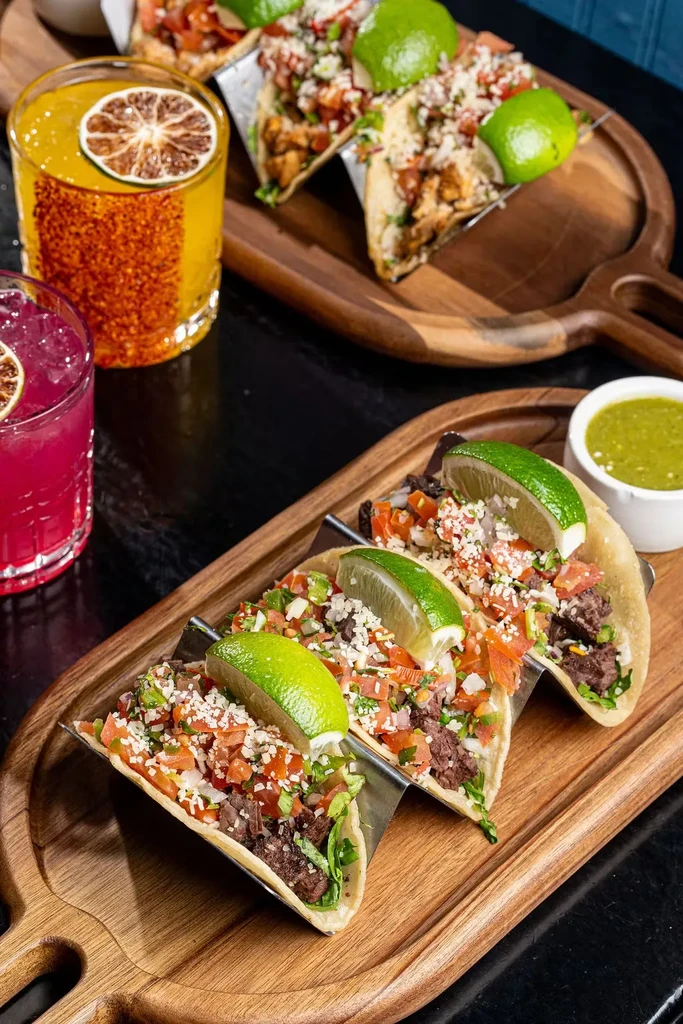 Three tacos with meat, pico de gallo, cheese, and a lime slice.
