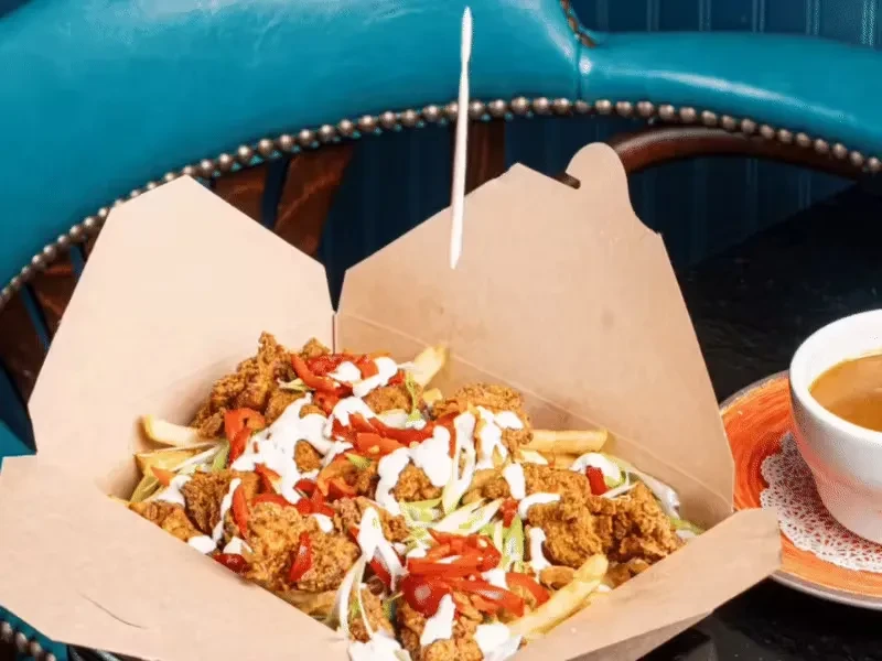 A takeout box filled with fried chicken, fries, red peppers, and sauce.