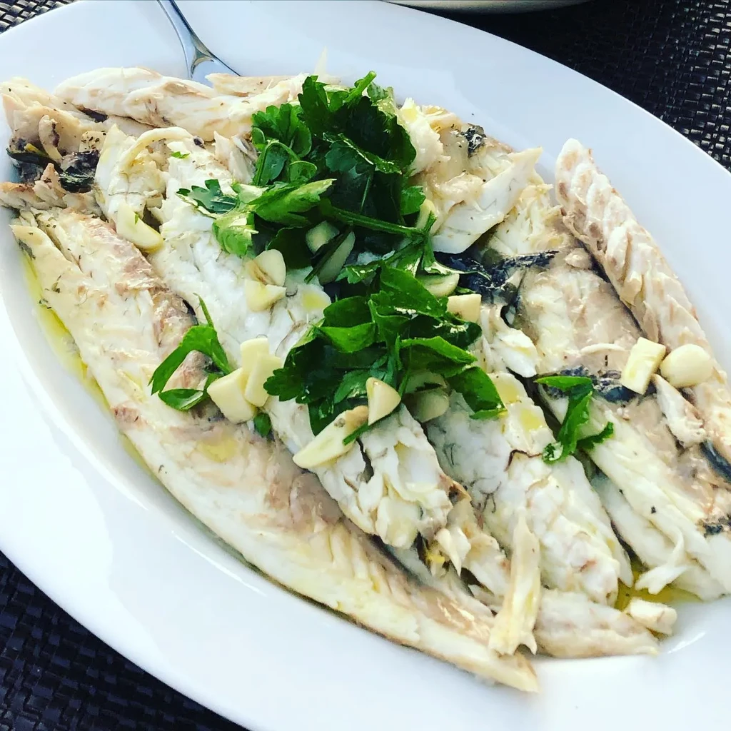 Steamed fish fillets with chopped parsley and garlic on a white plate.