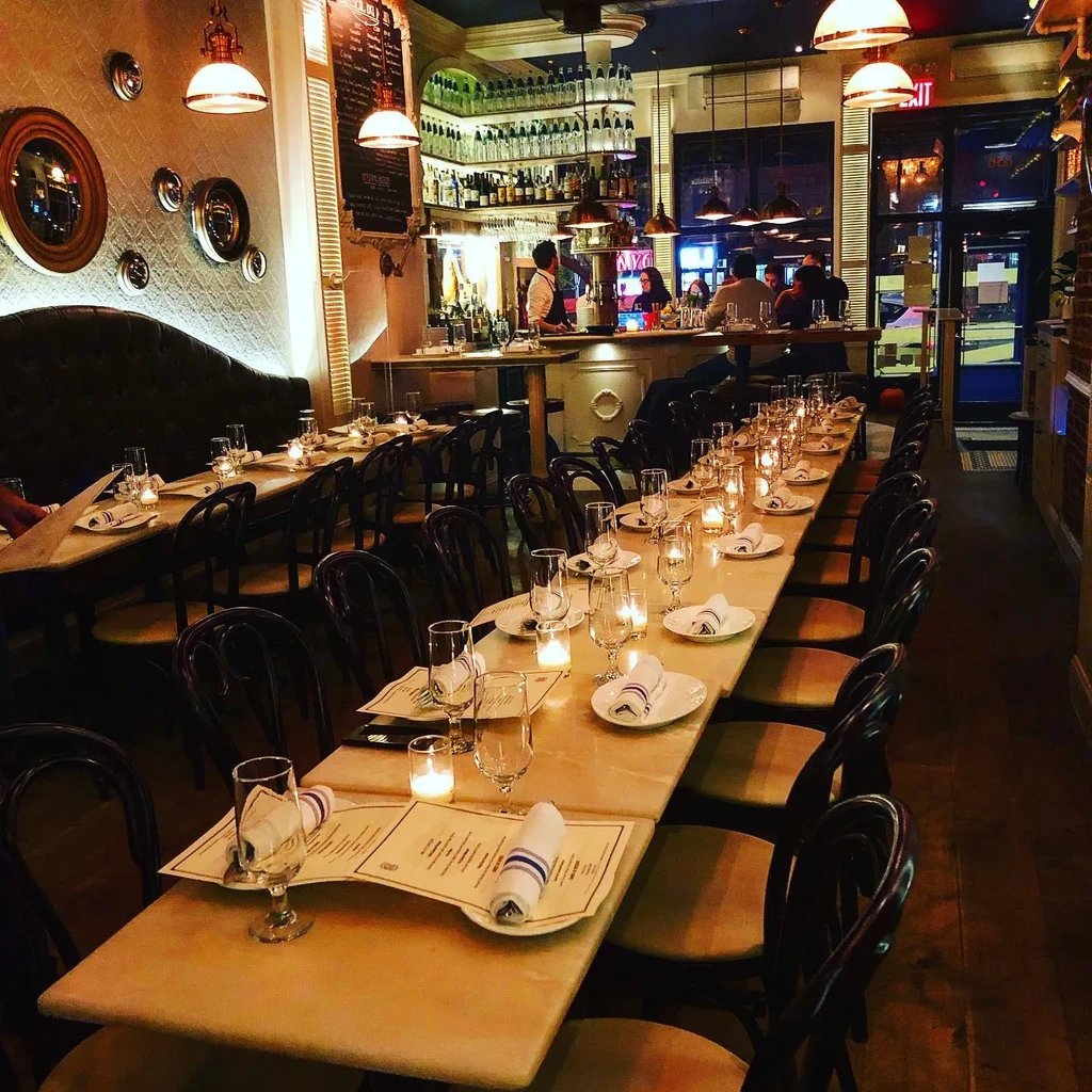 An empty restaurant dining room at night with tables set and a bar.