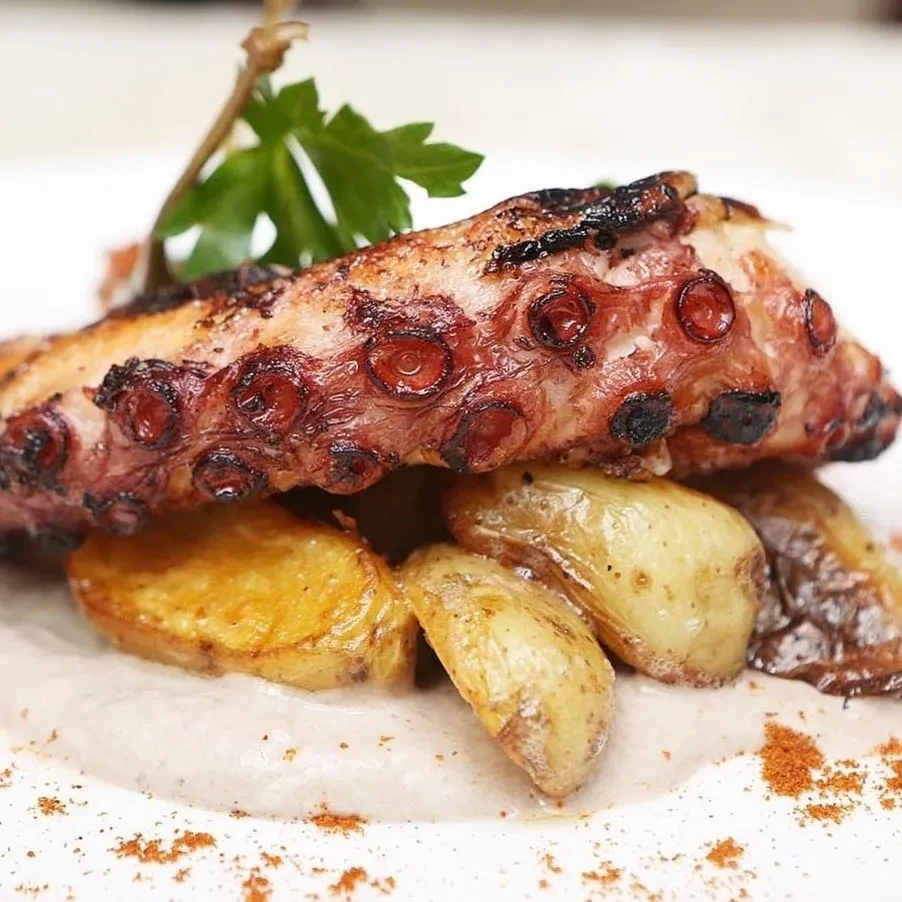 Grilled octopus tentacle with roasted potatoes on a white plate.