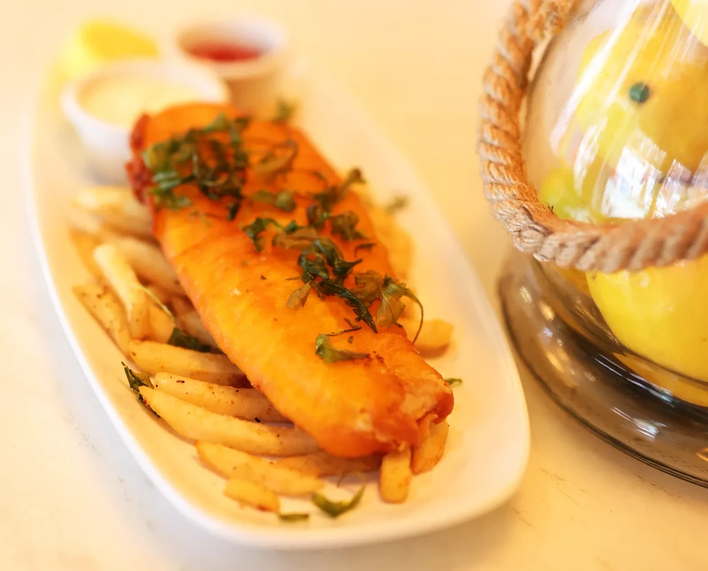 Fish and chips with sauces and a lemon wedge on a plate.