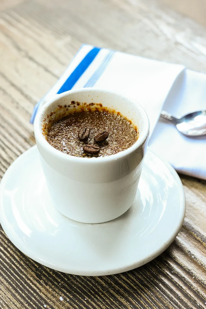 A white cup of crème brûlée with three coffee beans on top.