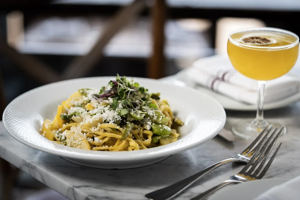 Pasta with vegetables and cheese, a drink, and forks on a marble table.