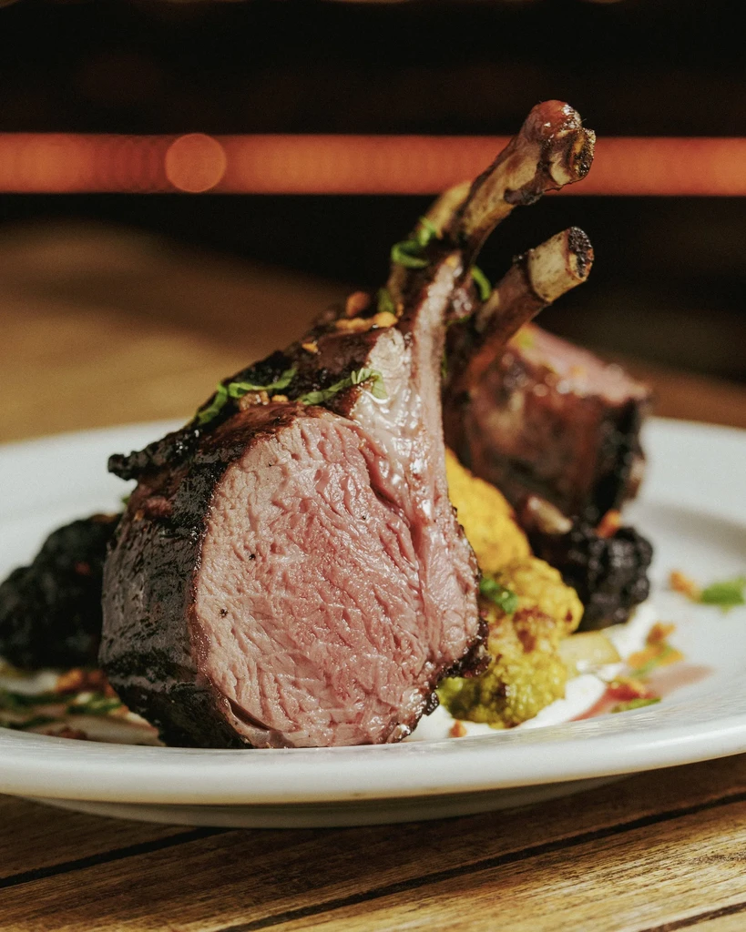 Two lamb chops, cooked rare, on a white plate with vegetables.