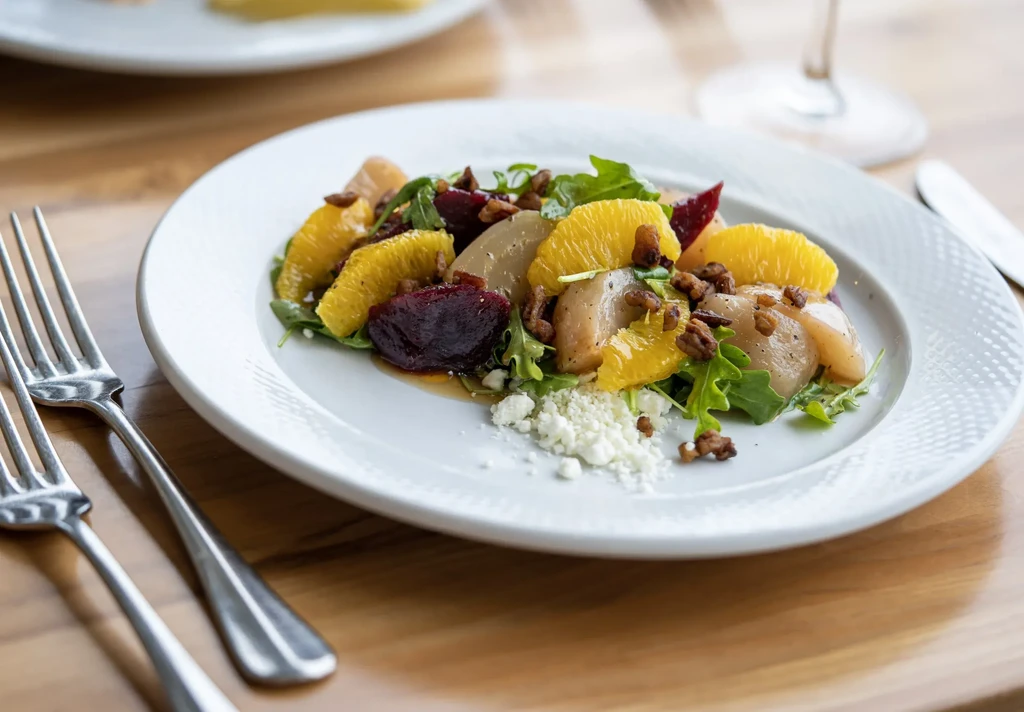 Salad with oranges, beets, pears, walnuts, and cheese on a white plate.