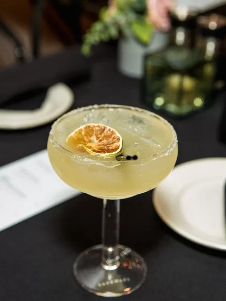 A margarita with a lime slice and salted rim on a black table.